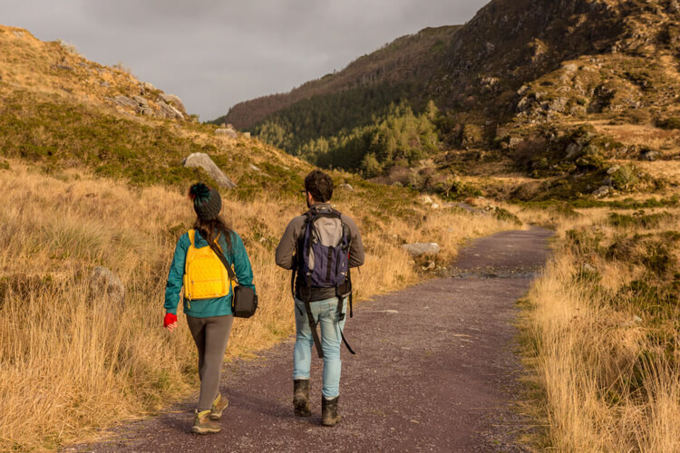 a young man and woman with backpacks walkling a gravel trail in the mountains during aumtumn