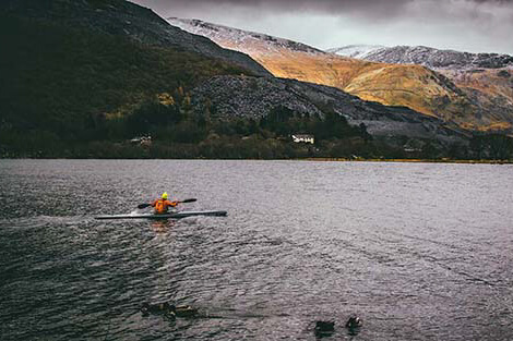 single person in a kayak paddling in a lake with snow-capped mountains in the background
