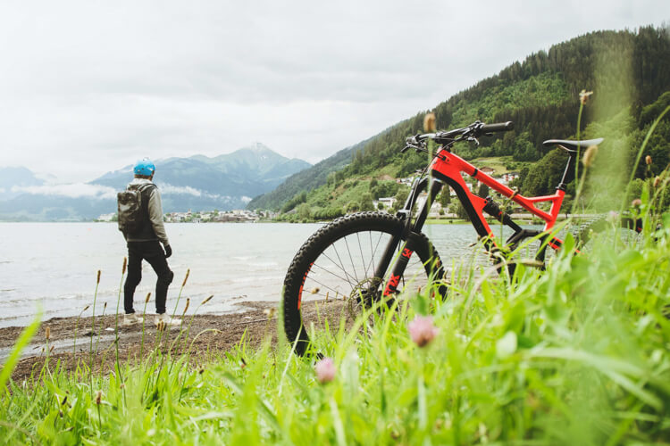 a bike parked in the grass beside a lake, with a man in the background
